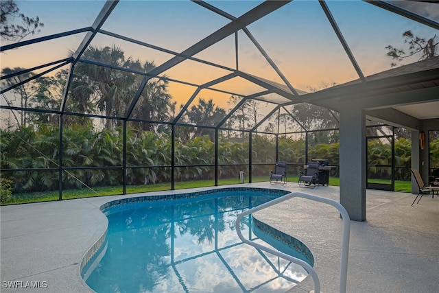 pool at dusk featuring glass enclosure and a patio area