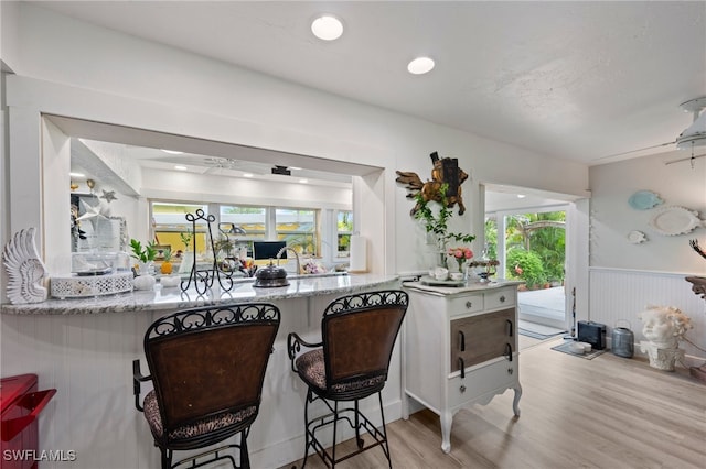 kitchen with light stone counters, ceiling fan, and light wood-type flooring