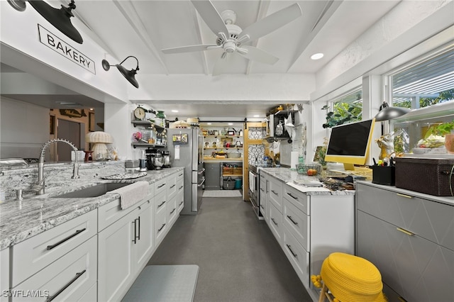 kitchen featuring appliances with stainless steel finishes, sink, white cabinets, ceiling fan, and light stone counters