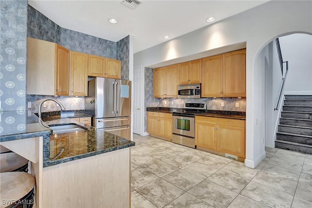 kitchen with sink, backsplash, stainless steel appliances, and dark stone counters