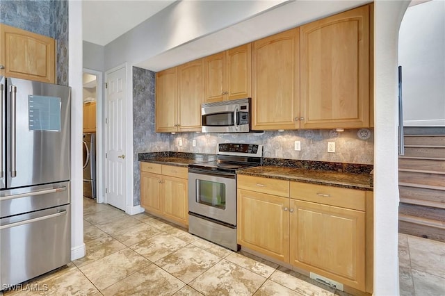 kitchen with light tile patterned floors, stainless steel appliances, tasteful backsplash, dark stone counters, and light brown cabinets