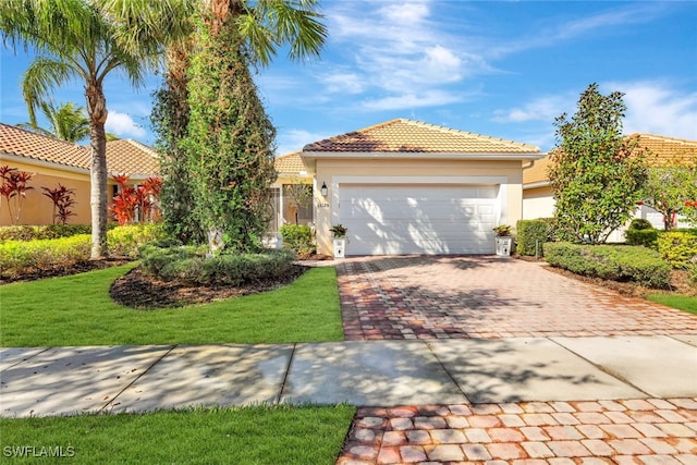 view of front of home with a garage, a tiled roof, decorative driveway, a front yard, and stucco siding