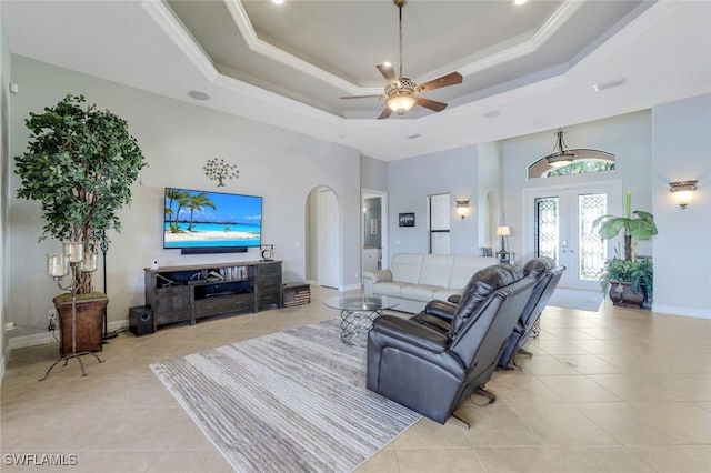 tiled living room featuring french doors, ornamental molding, ceiling fan, and a tray ceiling