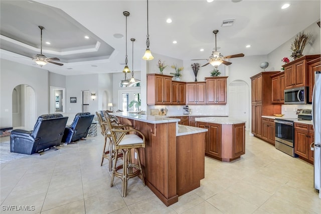 kitchen with stainless steel appliances, a center island, a raised ceiling, a kitchen bar, and kitchen peninsula