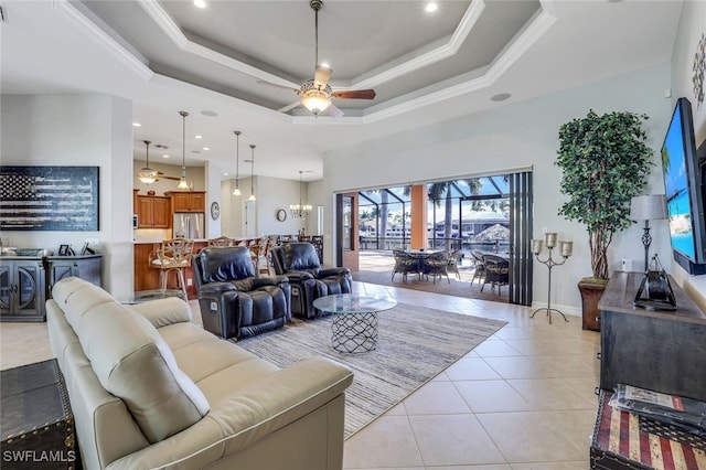 living room with light tile patterned floors, a tray ceiling, ceiling fan with notable chandelier, and ornamental molding