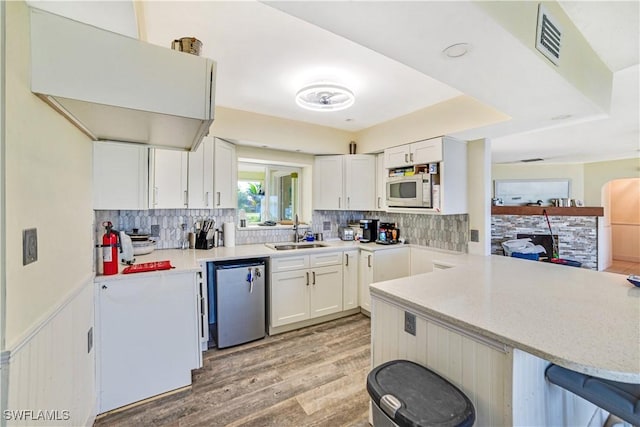 kitchen with sink, a breakfast bar area, white cabinetry, dishwasher, and kitchen peninsula