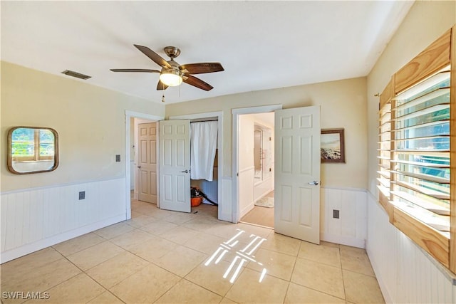 unfurnished bedroom with multiple windows, light tile patterned flooring, ceiling fan, and ensuite bath