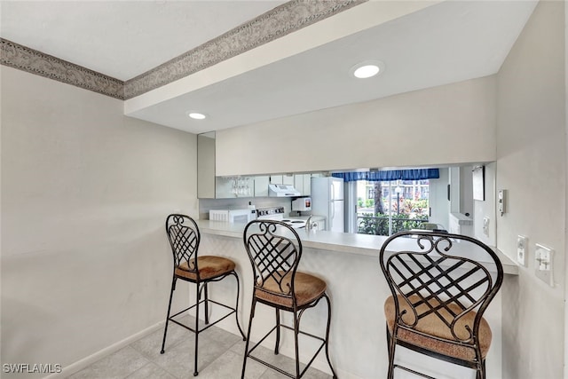 kitchen featuring white appliances, a breakfast bar, gray cabinets, and kitchen peninsula