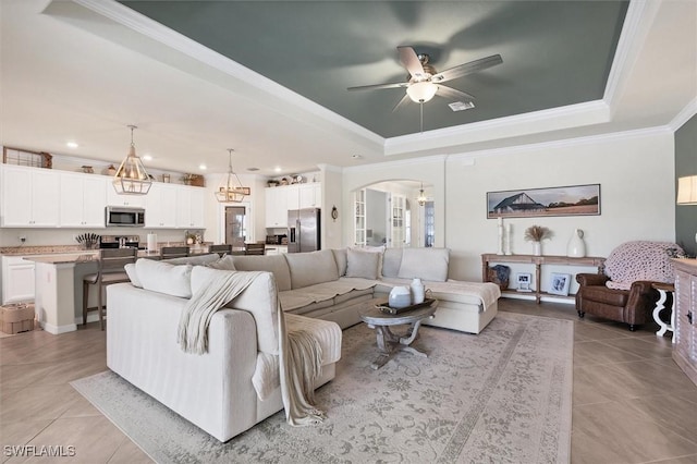 tiled living room with crown molding, a tray ceiling, and ceiling fan with notable chandelier