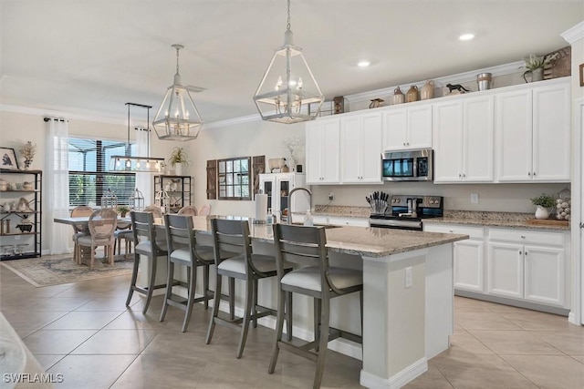 kitchen featuring pendant lighting, white cabinetry, ornamental molding, stainless steel appliances, and a center island with sink