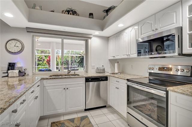 kitchen with appliances with stainless steel finishes, light tile patterned flooring, a sink, and white cabinets