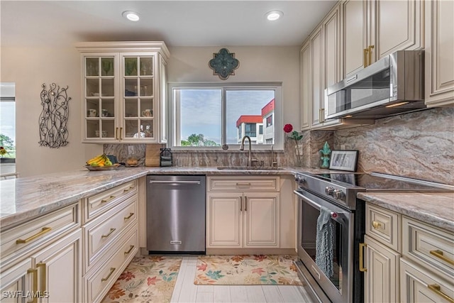 kitchen featuring sink, backsplash, stainless steel appliances, cream cabinets, and light stone countertops