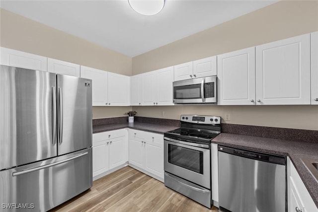 kitchen featuring stainless steel appliances, light wood-style floors, dark countertops, and white cabinets