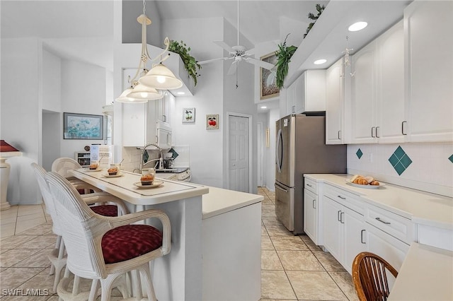 kitchen featuring stainless steel fridge, ceiling fan, decorative backsplash, white cabinets, and decorative light fixtures