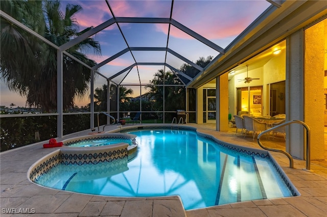 pool at dusk featuring an in ground hot tub, a patio, ceiling fan, and glass enclosure