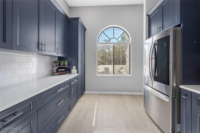 kitchen featuring stainless steel refrigerator, light hardwood / wood-style floors, blue cabinetry, and tasteful backsplash