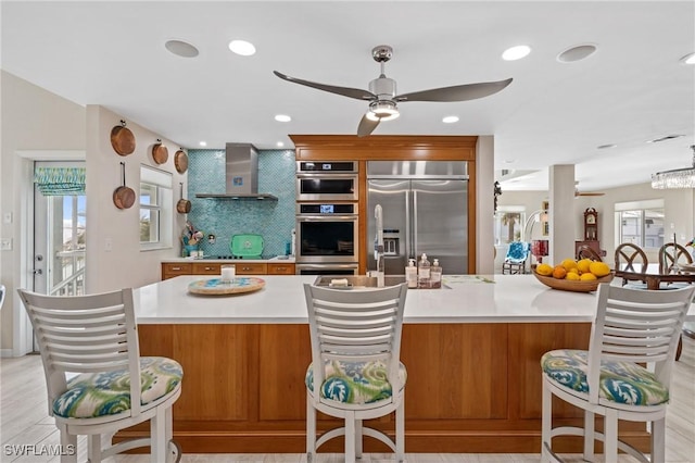 kitchen featuring a spacious island, appliances with stainless steel finishes, ceiling fan, decorative backsplash, and wall chimney range hood