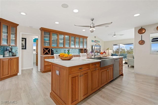 kitchen with stainless steel dishwasher, a center island with sink, backsplash, and light hardwood / wood-style flooring