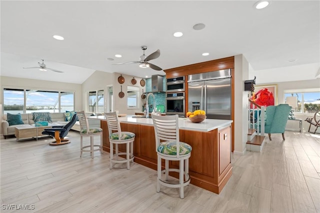 kitchen with appliances with stainless steel finishes, a breakfast bar, light hardwood / wood-style floors, and a center island with sink