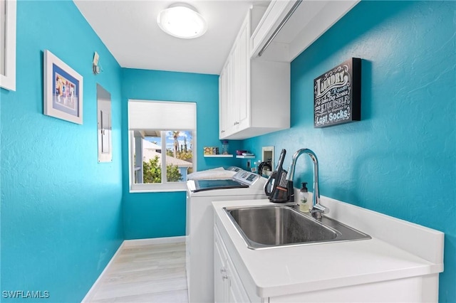 clothes washing area with sink, light hardwood / wood-style floors, cabinets, and washing machine and clothes dryer