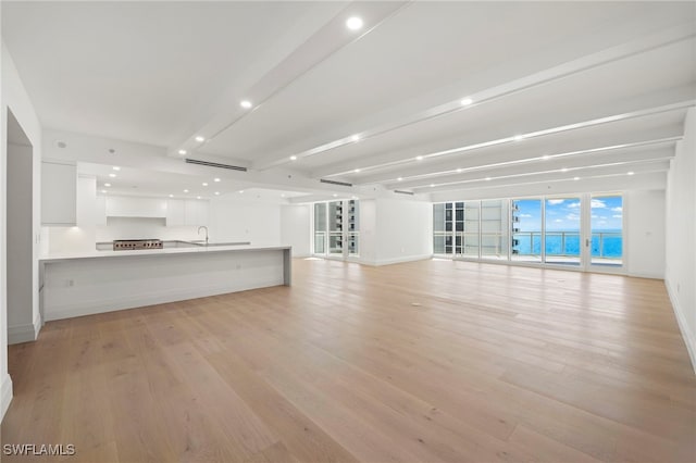 unfurnished living room with beam ceiling, sink, and light wood-type flooring