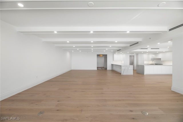 spare room featuring sink, light hardwood / wood-style flooring, and beamed ceiling