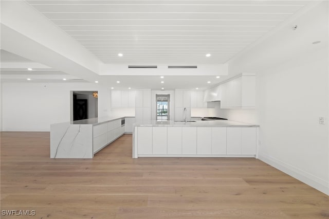 kitchen with white cabinetry, wall chimney range hood, light stone countertops, and light wood-type flooring