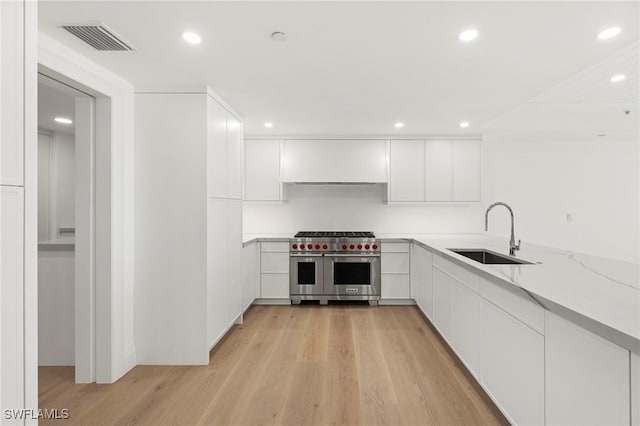 kitchen featuring sink, white cabinetry, range with two ovens, light stone counters, and light wood-type flooring