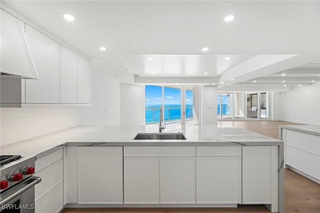 kitchen featuring stainless steel stove, sink, white cabinets, and custom range hood