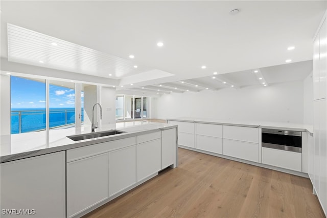 kitchen featuring white cabinetry, a water view, sink, and light hardwood / wood-style flooring