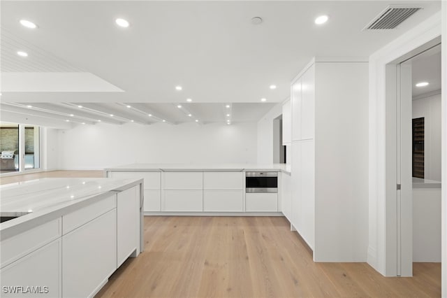 kitchen featuring oven, light wood-type flooring, light stone countertops, and white cabinets