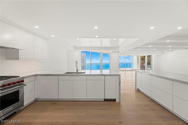 kitchen featuring sink, luxury stove, light hardwood / wood-style flooring, kitchen peninsula, and white cabinets