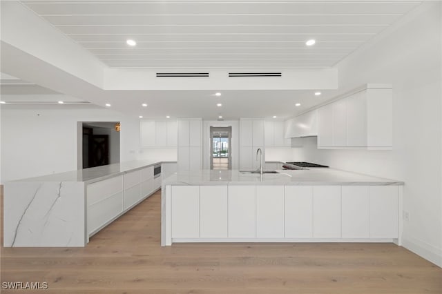 kitchen with light stone countertops, sink, wall chimney range hood, and white cabinets