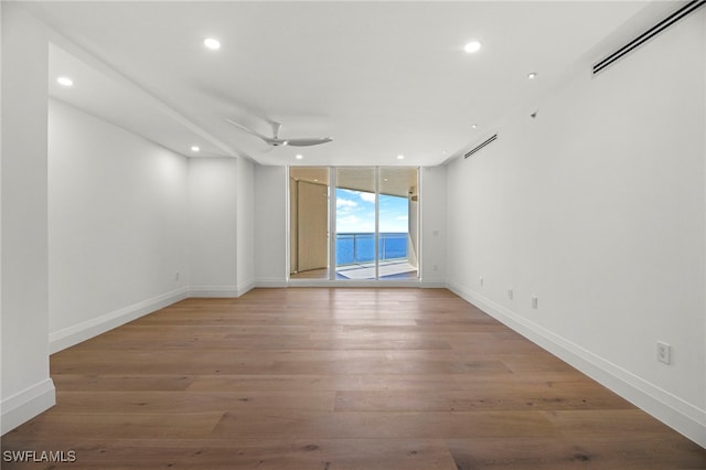 empty room featuring ceiling fan, a water view, light wood-type flooring, and a wall of windows