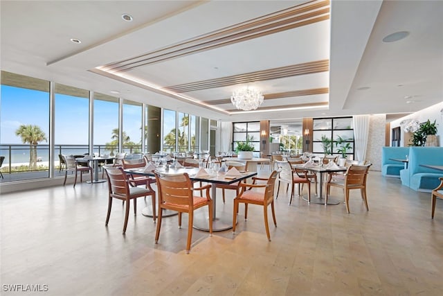 dining area with a raised ceiling, floor to ceiling windows, a water view, and an inviting chandelier