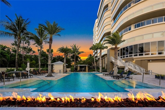 pool at dusk featuring an outdoor fire pit and a patio