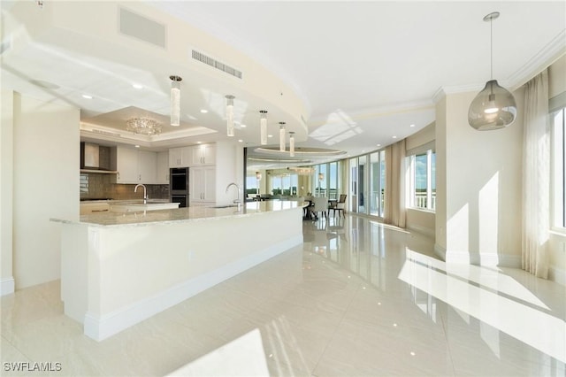 kitchen with wall chimney exhaust hood, visible vents, a sink, and ornamental molding