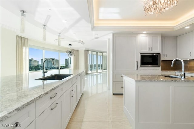 kitchen with built in microwave, a raised ceiling, a sink, and decorative backsplash