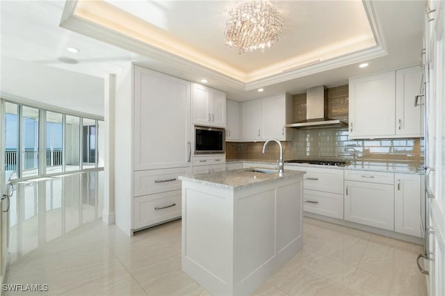 kitchen featuring built in microwave, a raised ceiling, a sink, and wall chimney range hood