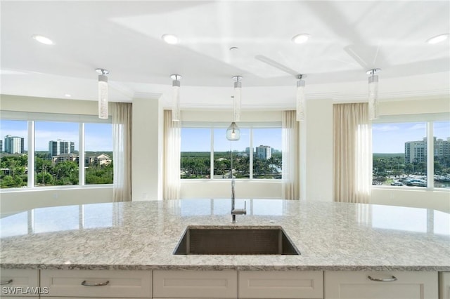 kitchen featuring a view of city, white cabinetry, a sink, light stone countertops, and plenty of natural light