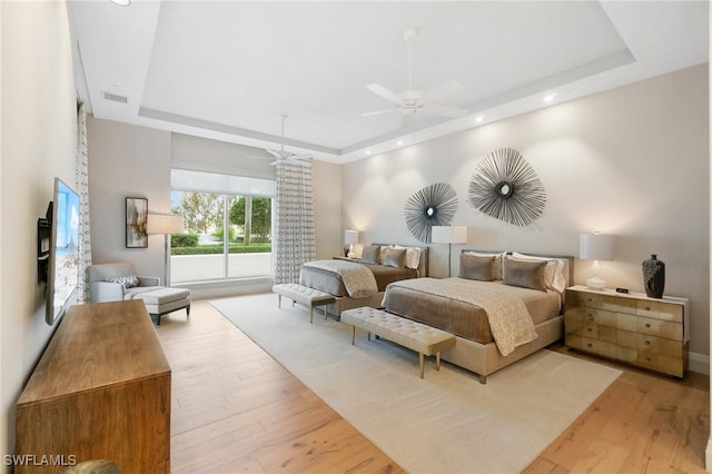 bedroom featuring light wood-style floors, a raised ceiling, visible vents, and a ceiling fan