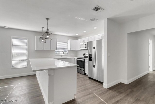 779 108th Ave N, Naples, FL 34108 - kitchen featuring appliances with stainless steel finishes, hardwood / wood-style floors, pendant lighting, white cabinets, and kitchen peninsula