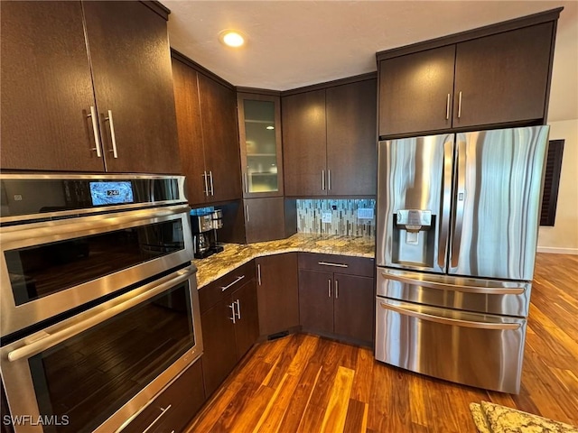 kitchen featuring dark brown cabinetry, dark hardwood / wood-style flooring, appliances with stainless steel finishes, and light stone counters