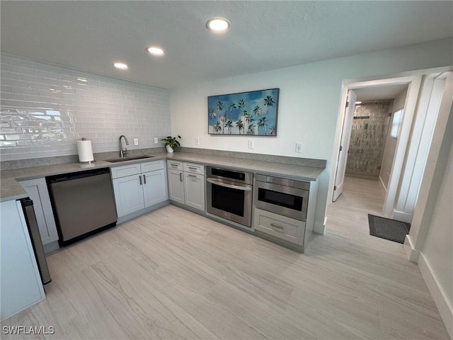 kitchen with tasteful backsplash, sink, stainless steel appliances, and light hardwood / wood-style floors