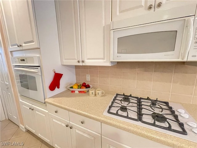 kitchen featuring tasteful backsplash, light tile patterned floors, white cabinets, and white appliances