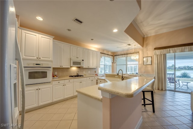 kitchen with white appliances, an island with sink, a sink, and white cabinetry