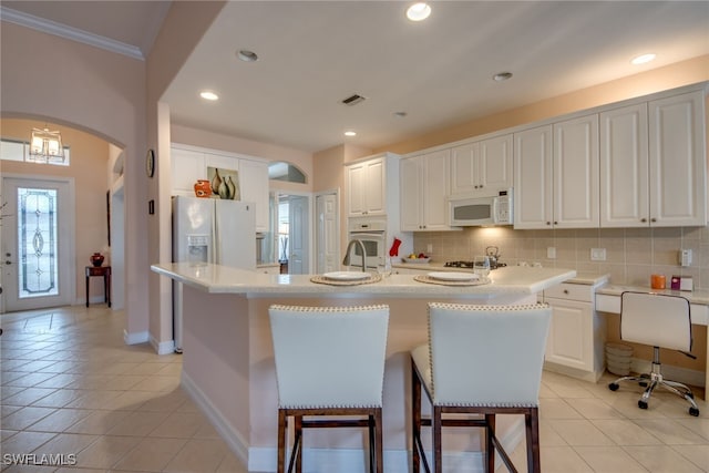 kitchen featuring white cabinets, white appliances, a center island with sink, and light countertops