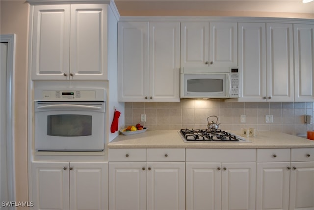 kitchen with white appliances, backsplash, white cabinets, and light countertops