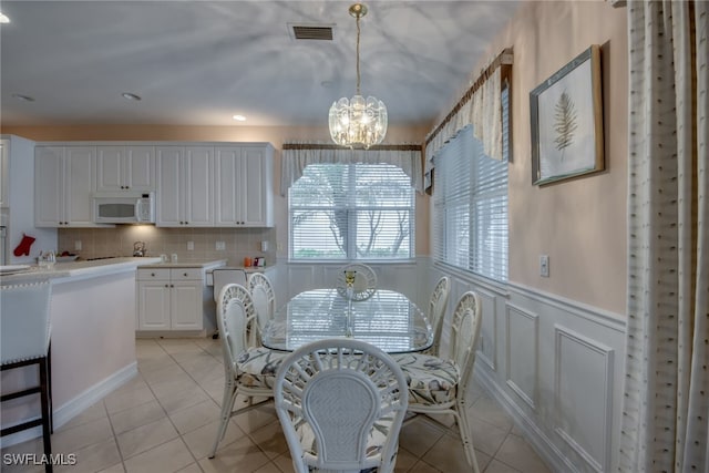 dining area with light tile patterned floors, visible vents, a decorative wall, wainscoting, and a chandelier