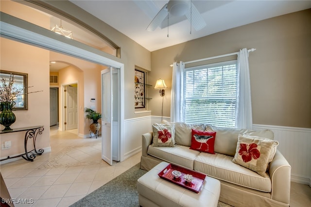 living area with a wainscoted wall, light tile patterned floors, arched walkways, and a ceiling fan